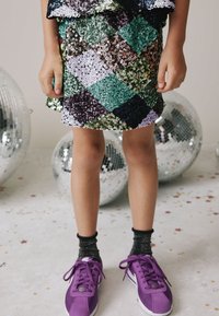 Robe à sequins avec un motif en losanges aux tons verts, violets et argentés, accompagnée de baskets violettes et de chaussettes noires scintillantes.
