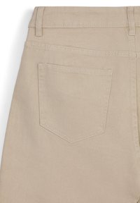 Tessuto di denim beige caratterizzato da una tasca posteriore con un sottile motivo di cucitura contornato. La texture è liscia con una leggera elasticità.