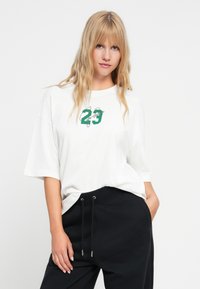 Balta per didelė marškinė su žalia grafika, kurioje yra "23" centre. Vardinta su juodomis džinsinėmis kelnėmis su raišteliu ir šoninėmis kišenėmis.