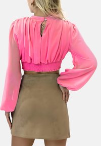 Roze, semi-doorschijnende cropped blouse met lange mouwen, smugged tailleband en sleufdetail aan de achterkant, gecombineerd met een beige suède minirok.