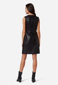 Robe sans manches en cuir noir avec une silhouette ajustée, un col montant et une fermeture éclair au dos. Texture lisse avec un design épuré.