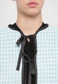 Tekstuuriga sinine ja valge ruuduline kangas jakk mustade satiinipatjadega kaelas ja musta kontrastse kangaga all.