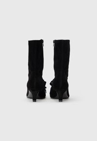 Μαύρα μποτάκια αστραγάλου από σουέντ με στενό τακούνι, κλείσιμο με φερμουάρ και διακοσμητικό φιόγκο στο πλάι. Διαθέτουν λεία υφή και κομψό, γραμμικό σχήμα.