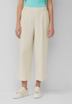 Lichtbeige, loszittende, cropped broek met een gestructureerde stof, elastische tailleband en voorplooien, gecombineerd met off-white sneakers.
