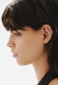 Pendiente de banda múltiple de plata llevado en la oreja de un modelo, con líneas elegantes y una textura pulida, sobre un fondo claro.