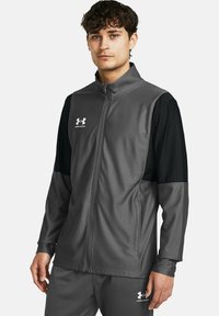 Grau und schwarze Zip-Jacke aus glattem Stoff, mit hohem Kragen und Seitentaschen; Under Armour-Logo auf der Brust.