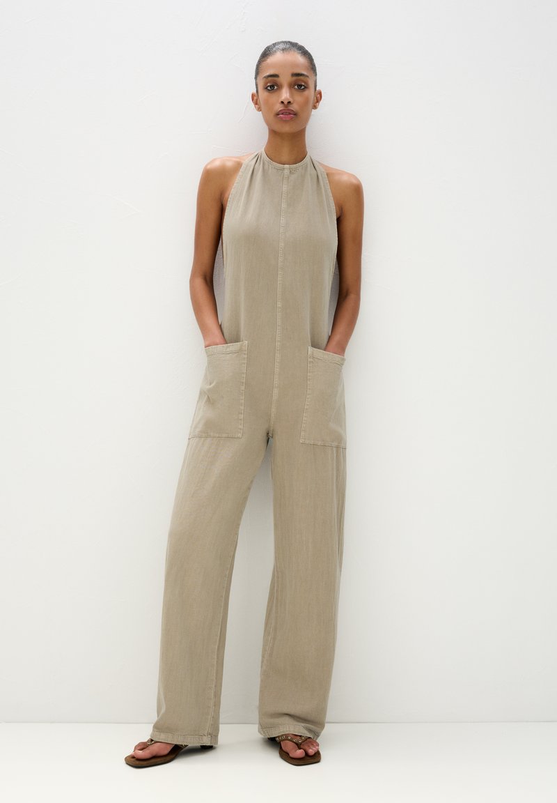 Beige Jumpsuit aus leichtem Stoff mit Halterneck, vorderem Knopfverschluss, zwei großen Taschen und weitem Bein. Strukturierte Oberfläche.