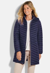 Marineblauwe pufferjas met chevron-quilting, een ritssluiting aan de voorkant en een capuchon. Lichtgewicht materiaal, knielange uitstraling en slim fit.