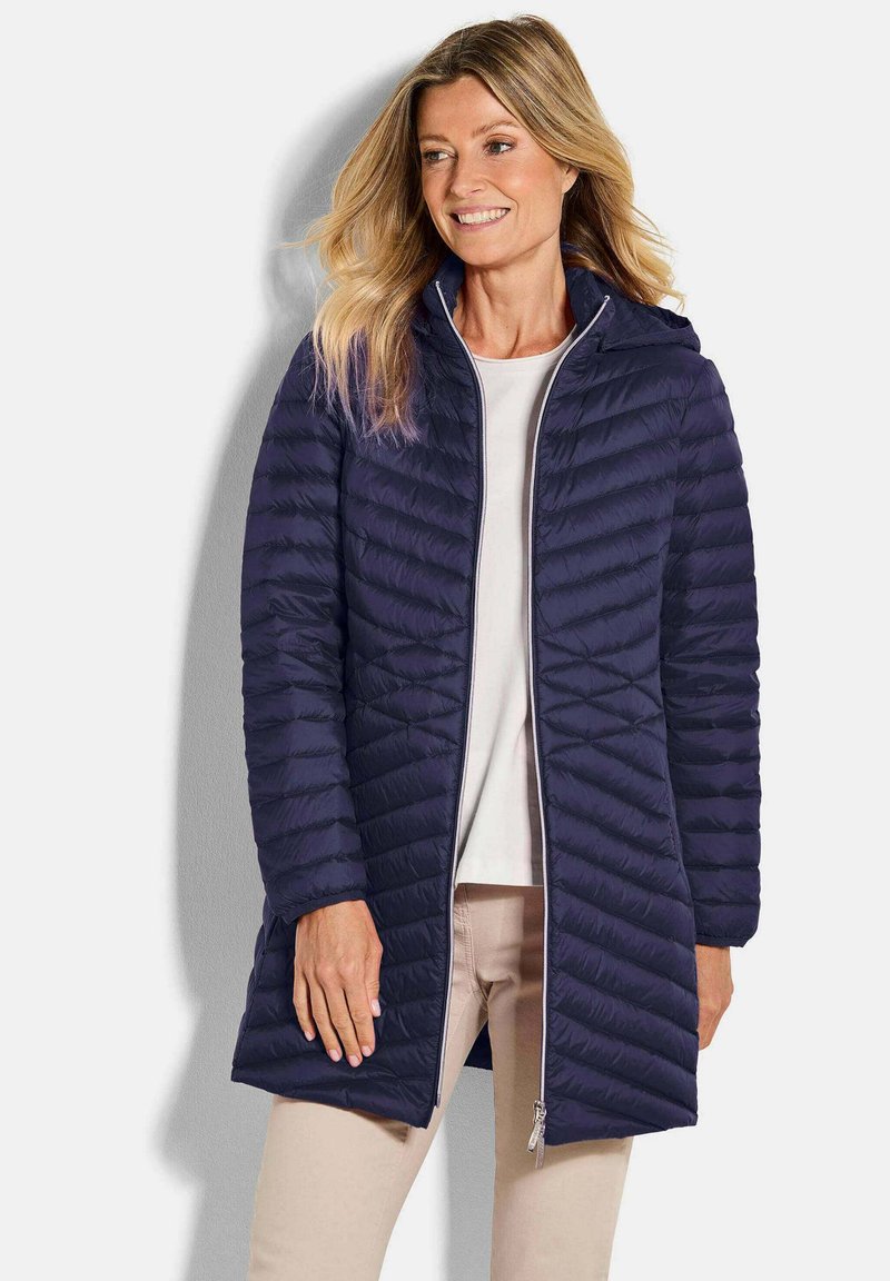 Marineblauwe pufferjas met chevron-quilting, een ritssluiting aan de voorkant en een capuchon. Lichtgewicht materiaal, knielange uitstraling en slim fit.