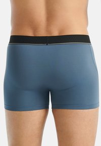 Herrarnas boxertrosor i matt blått tyg, med ett svart elastiskt midjeband med subtil grå sömnad. Slät textur, åtsittande design.