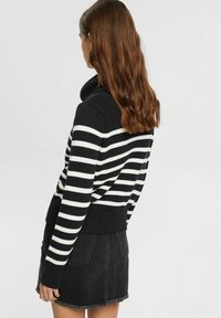 Schwarz-weißer gestreifter Rollkragenpullover mit geripptem Saum, kombiniert mit einem schwarzen Jeansrock mit fransigem Rand.