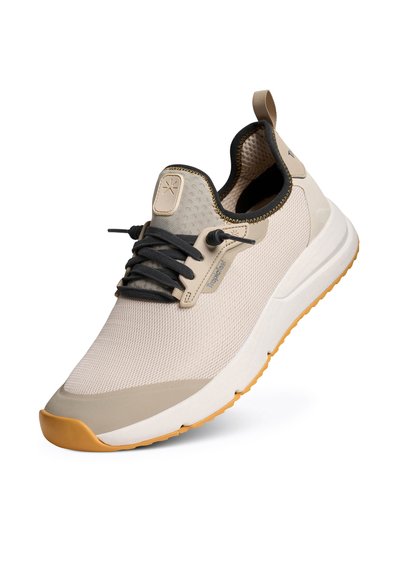 Baskets beige clair avec des lacets noirs et une semelle en caoutchouc couleur tan, dessus en mesh respirant et languette au talon pour un enfilage facile.