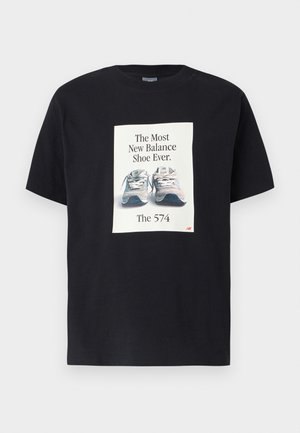 Zwart katoenen T-shirt met een grote witte afbeelding en tekst, en een afbeelding van New Balance 574 schoenen in tinten grijs en blauw.