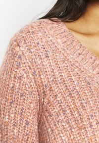 Rosa stickad tröja med en tjock textur och inslag av orange och blått, V-ringning och ribbat detaljer längs kanterna.