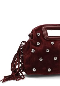 Bolso de ante rojo oscuro con tachuelas de metal, asa recortada y largas borlas en el lateral, sobre un fondo blanco.