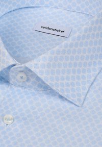 Chemise habillée bleu clair avec un motif géométrique subtil, boutons blancs et une étiquette « seidensticker » à l'intérieur du col.