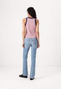 Débardeur rayé rouge et blanc avec des finitions bleu marine ; associé à un jean évasé bleu clair. Des chaussures noires complètent la tenue.