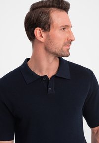 Polo shirt bleu marine à manches courtes avec un tricot texturé, doté d'un col classique, d'une patte de boutonnage à trois boutons et de poignets côtelés.