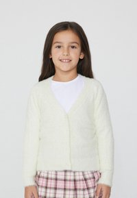 Flauschige, hellgelbe Strickjacke mit V-Ausschnitt und Knopfverschluss, die lange Ärmel und eine weiche Textur hat, kombiniert mit einem karierten Rock.