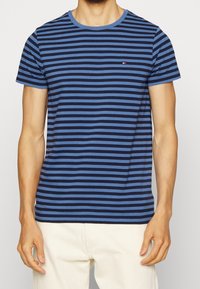 Námořnická modrá a modro pruhovaná tričko s krátkým rukávem vyrobené z měkké bavlny. Má kruhový výstřih a malé logo na hrudi.