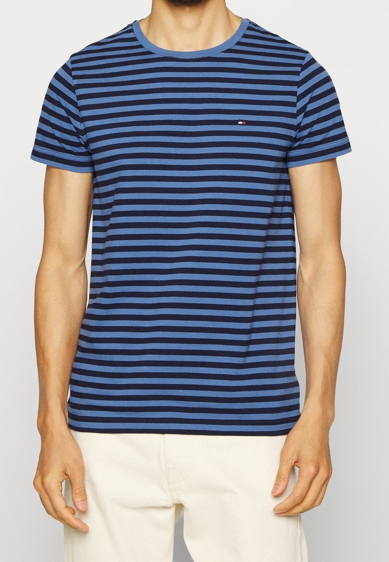 Námořnická modrá a modro pruhovaná tričko s krátkým rukávem vyrobené z měkké bavlny. Má kruhový výstřih a malé logo na hrudi.
