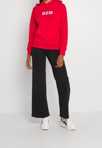 Sudadera roja con el logo blanco de "LEVI'S", que incluye un cordón, combinada con pantalones anchos negros y zapatillas blancas con acentos negros.