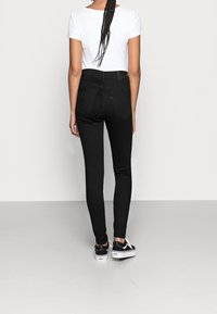 Vaqueros negros ajustados de cintura alta, con dos bolsillos traseros y una textura suave. Combinados con una blusa blanca de manga corta y zapatillas negras.