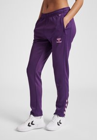 Paarse sportbroek met een elastische tailleband, zijzakken en een roze logo-detail. Gecombineerd met witte schoenen met zwarte accenten.