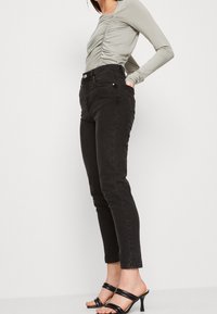 Jeans neri a vita alta con una vestibilità slim, dotati di chiusura con bottone, cinque tasche e una lunghezza cropped. Abbinati a un top a maniche lunghe con arricciature.