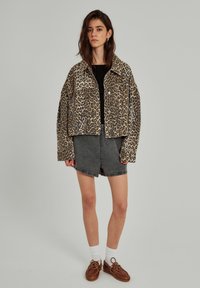 Leopard-print cropped jacket with a button front, paired with a black top, grey denim shorts, white socks, and brown lace-up shoes.