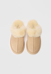 Beige suede tøfler med en luftig, kremfarget faux pelskant. Rund tådesign med en detaljert søm på overdelen. Myk tekstur.