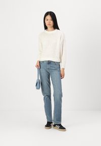 Cream knitted sweater with a round neckline, paired with light blue straight-leg jeans and black sneakers with white stripes. Light blue handbag.