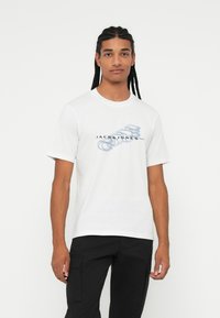 T-shirt bianco in cotone con testo grafico blu "JACK & JONES" sul petto. Maniche corte e scollo rotondo.