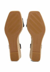 Sandali wedge neri con suola in gomma tan texturizzata; il tacco presenta dettagli in juta intrecciata e un design semplice con due cinturini regolabili.