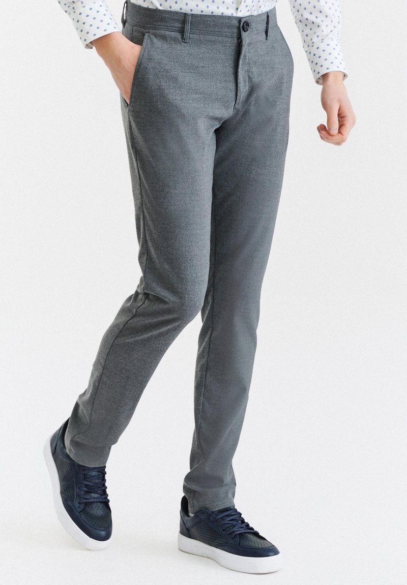 Szare, plecione spodnie o slim fit, z bocznymi kieszeniami i gładką fakturą, w połączeniu z ciemnonawigacyjnymi trampkami i wzorzystą koszulą.