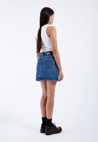 Gonna di denim corta con orlo sfilacciato, due tasche posteriori e etichetta in vita nera, abbinata a scarpe nere e calzini alla caviglia.