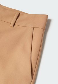 Pantalons beige ajustés avec une texture de tissu lisse, présentant un devant plat, deux plis sur le devant et une taille étroite avec une passante pour la ceinture.