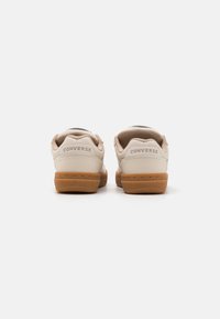 Beige bőr sneaker, texturált felülettel, gumiból készült talppal és domború márkareggel a saroknál. Lekerekített hátsó forma.