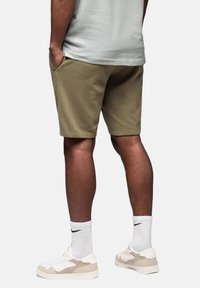 Shorts en coton vert olive avec poches latérales, coupe décontractée et ourlet cousu. Associés à des chaussettes blanches et des baskets beige.