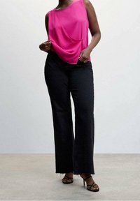 Haut fuchsia sans manches avec un design drapé, associé à un jean noir à jambes larges avec des bords effilochés et des talons noirs à brides.