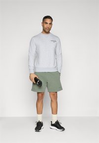 Gray sweatshirt with crew neck and black text logo, paired with olive green shorts. Black sneakers and light-colored socks complete the outfit.