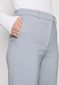 Jasnoniebieskie spodnie o kroju dopasowanym, wykonane z gładkiego materiału, z płaskim przodem, bocznymi kieszeniami i smukłym fasonem.