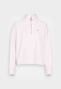 Sudadera de color rosa claro con cuello alto, cremallera de cuarto y detalles dorados. Presenta un pequeño logotipo en el pecho y puños acanalados.