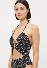 Schwarzes Blumenbikini mit Halterneck-Design, ausgeschnittenen Seiten, gerafftem Stoff und kleinen weißen und rosafarbenen Blumenmustern.