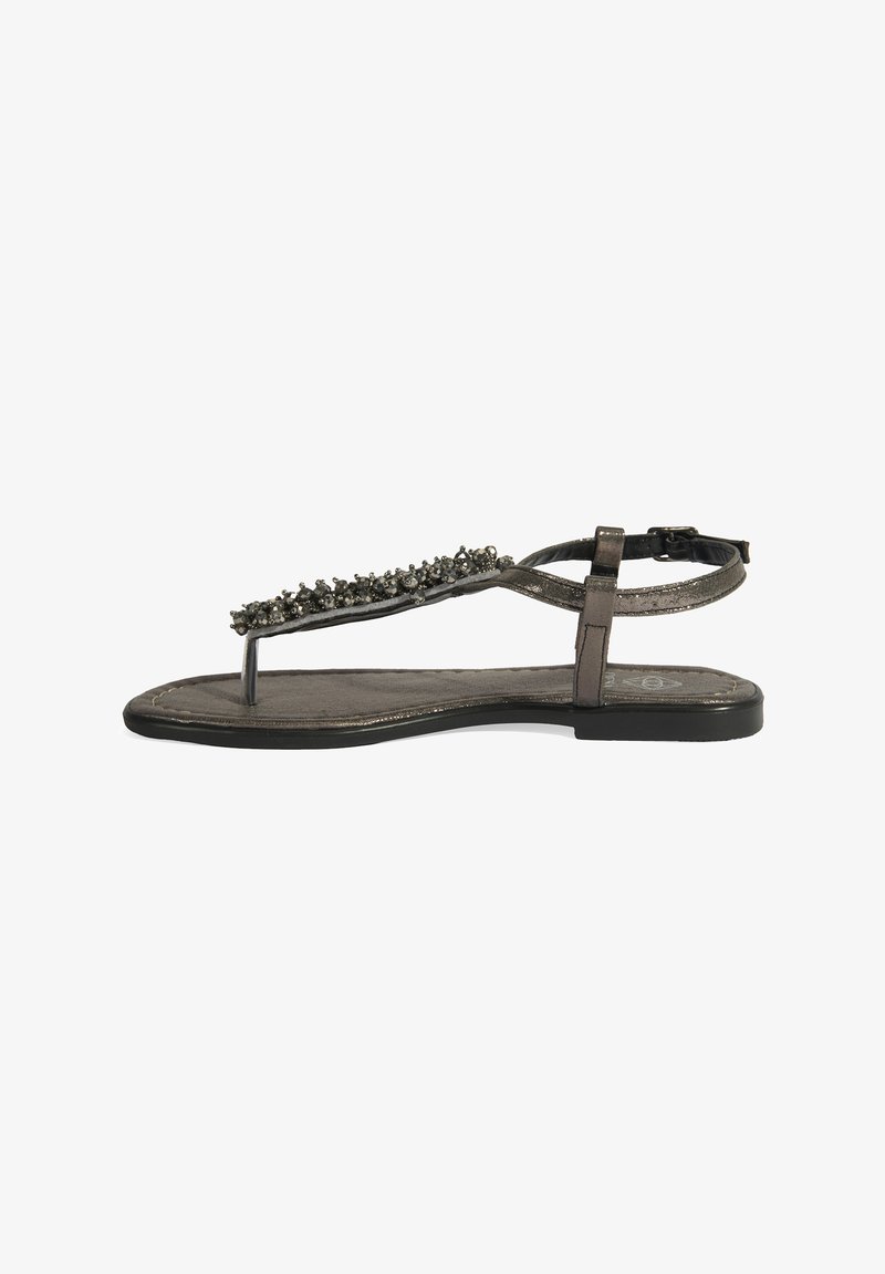 Sandal en métal gris avec un design à lanière en T, présentant une rangée décorative de sombres ornements le long de la lanière, une semelle plate et une boucle à la cheville.