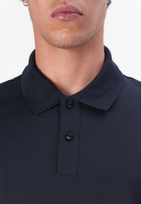 Tumes polo särk klassikalise krae, kolme nuppu ja tekstuurse kangaga. Peened detailid krael ja nupu aktsentidel.