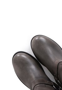 Botas de cuero gris con punta redonda y suelas negras, con un detalle de correa y hebilla de metal en el lateral, sobre un fondo blanco.
