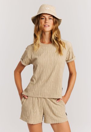 Beige terry stoffen outfit met een textuurrijke top met korte mouwen en bijpassende shorts, aangevuld met een beige buckethoed, allemaal voorzien van een golvend patroon.