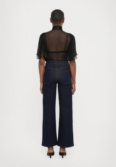 Black sheer blouse with short puff sleeves. Dark blue wide-leg jeans with a straight fit and back pockets. High-heeled black shoes.