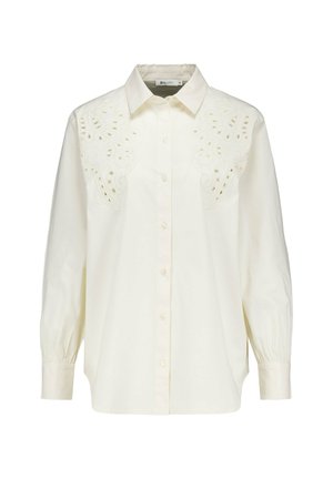 Chemise en coton blanche à manches longues, avec un devant à boutons et un design brodé complexe sur les épaules. Elle présente des poignets de manches froncés.